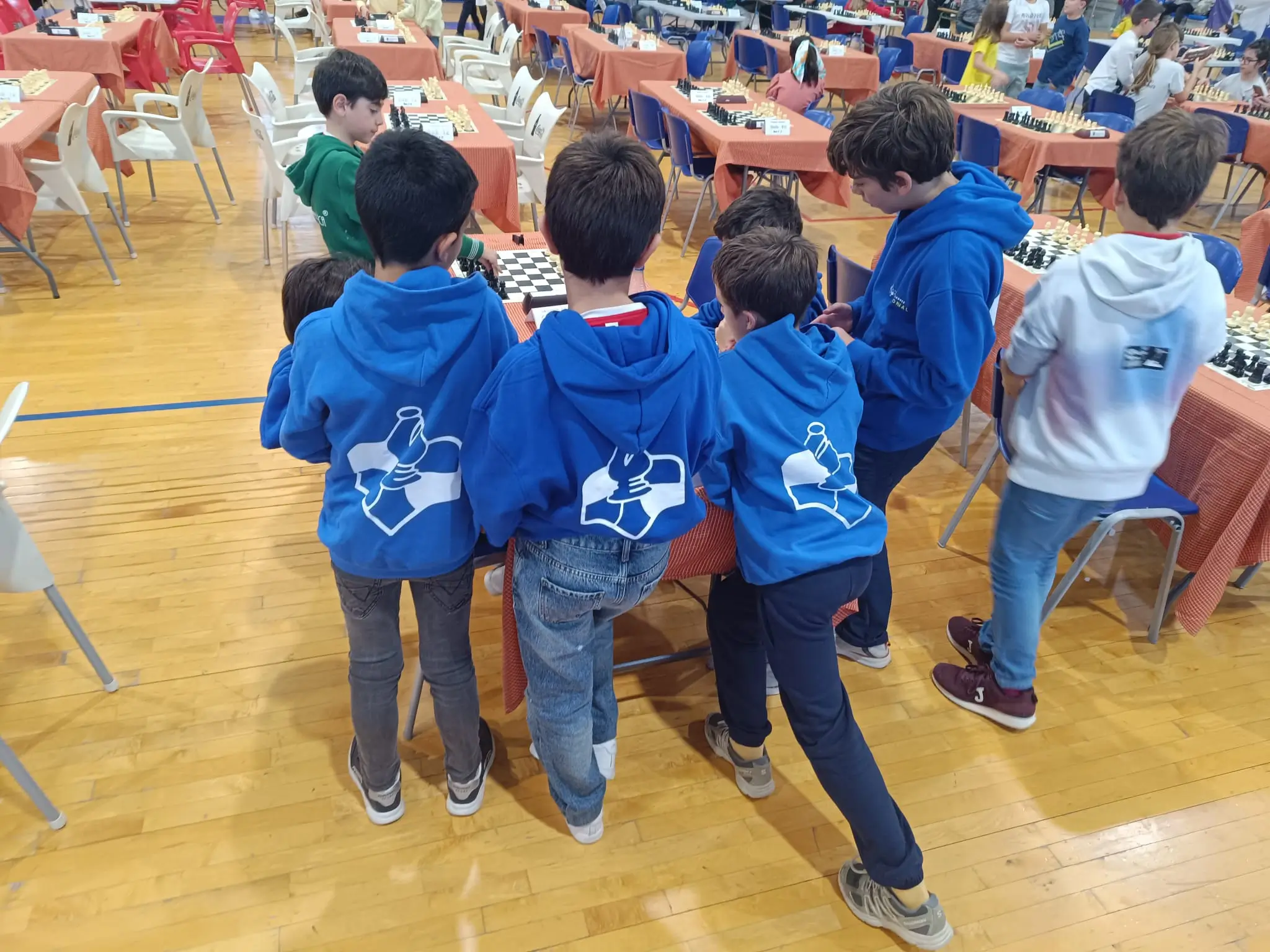 Niños con sudaderas del club mirando tableros de ajedrez en un torneo